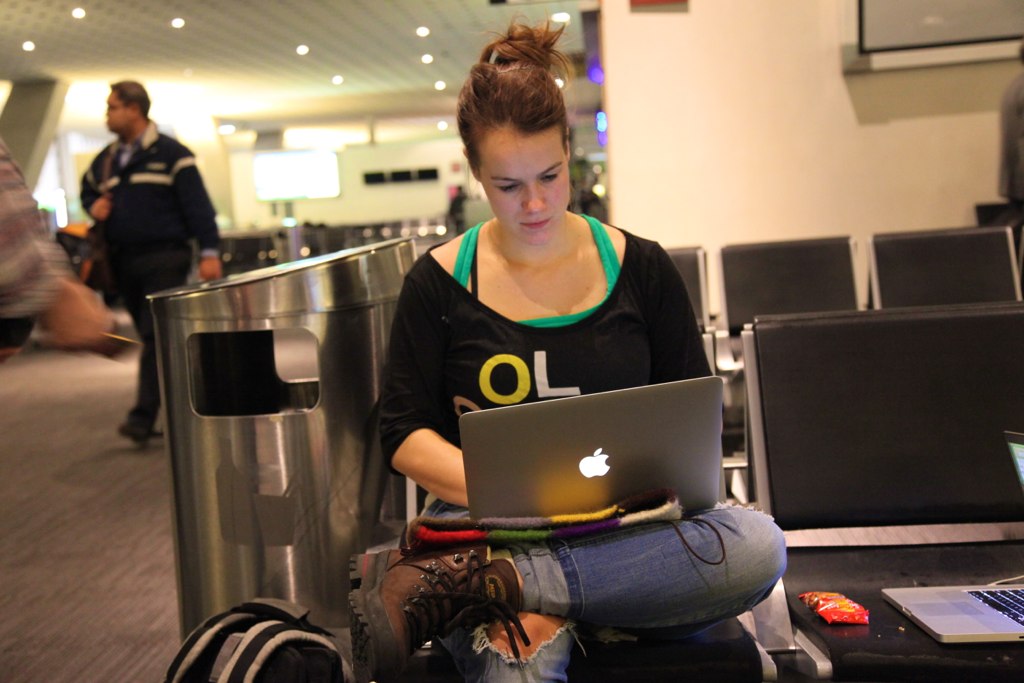 A lady working on her laptop in an airport. A digital nomad is someone who works remotely from anywhere in the world. Countries that offer digital nomad visa: Portugal, Estonia, Germany