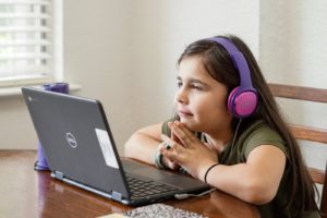 a little girl sitting at a table with a laptop. Cybersecurity, online safety