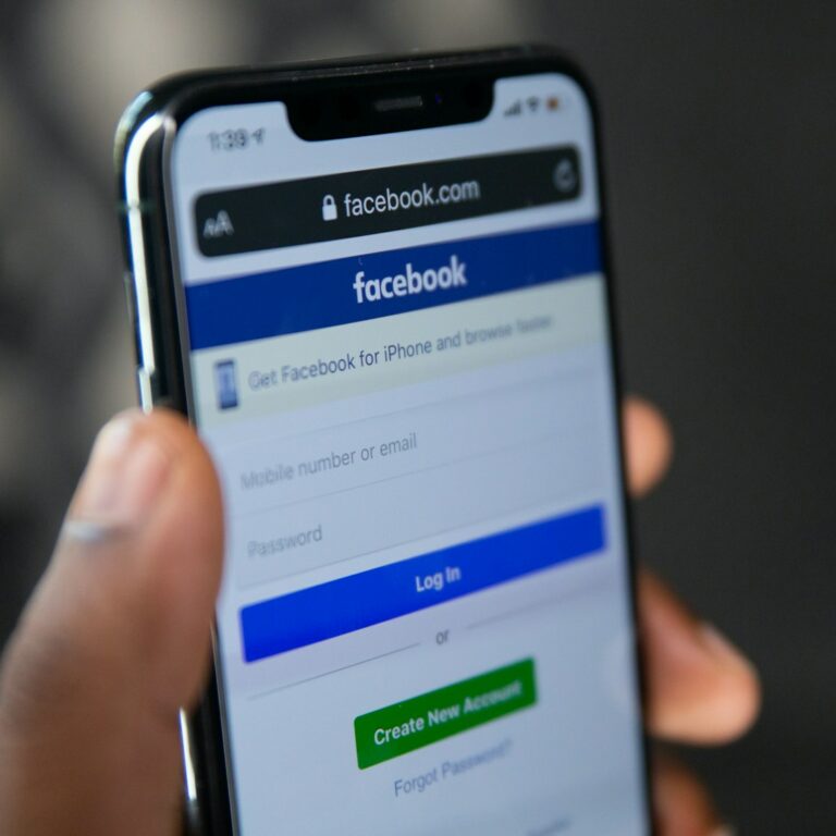 person holding silver iphone 6 with screen showing Facebook login, how to delete a Facebook Page